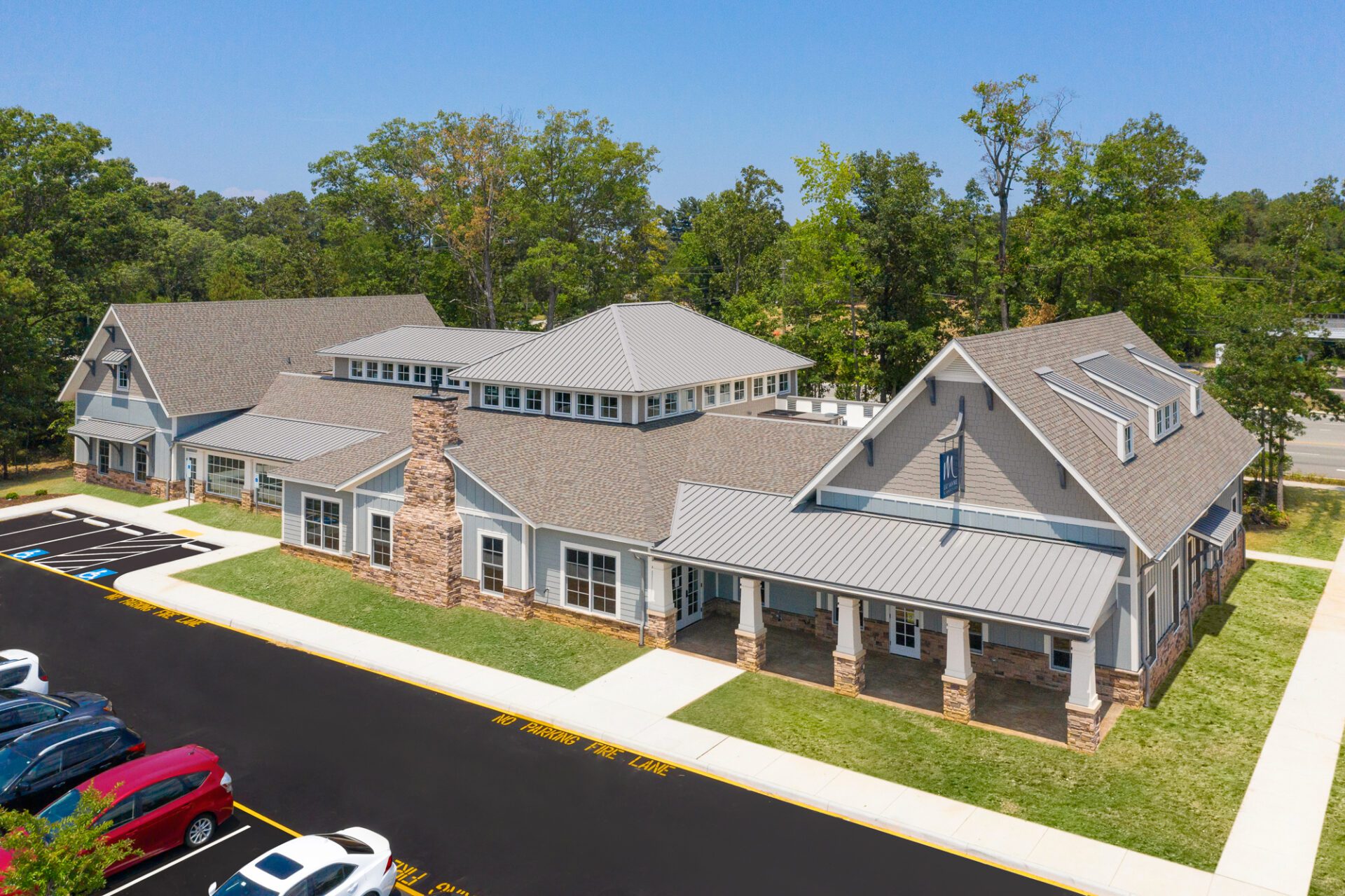 Aerial view of a modern suburban building with gray roofing and stone accents, surrounded by a parking lot