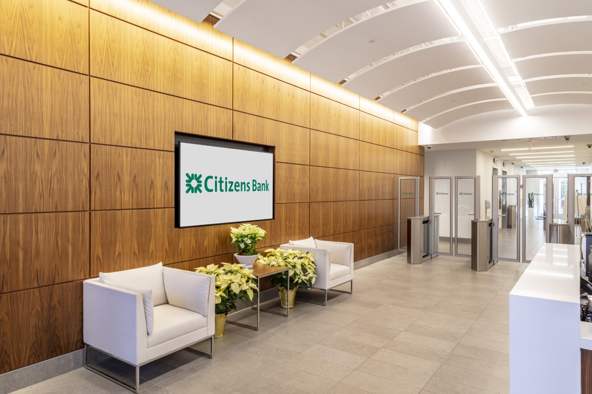 Modern bank lobby with wooden walls, a digital sign, seating area, and entrance turnstiles