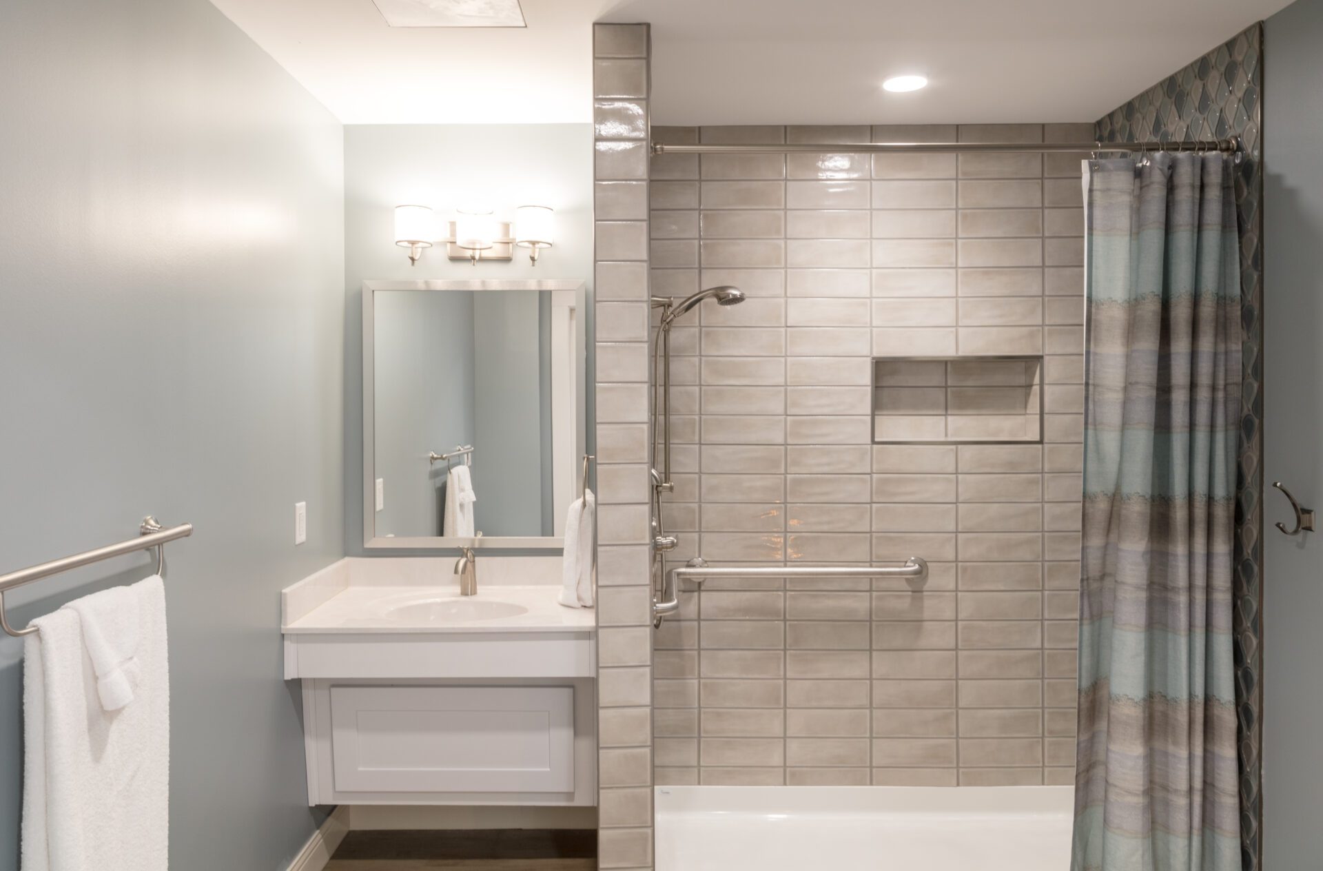 Modern bathroom with tiled walk-in shower, white vanity, and mirror with wall lights