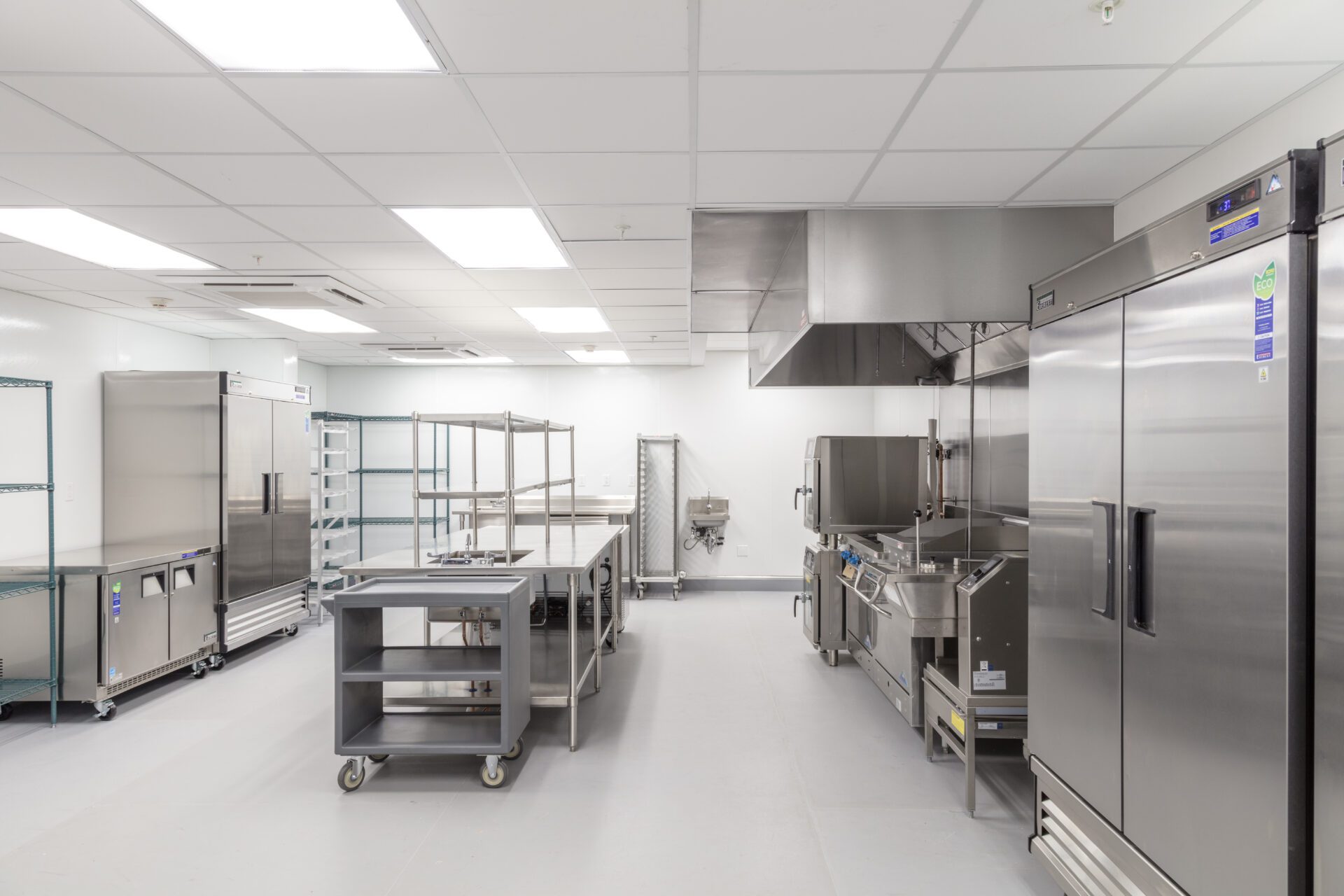 A clean and empty commercial kitchen with stainless steel equipment and white walls