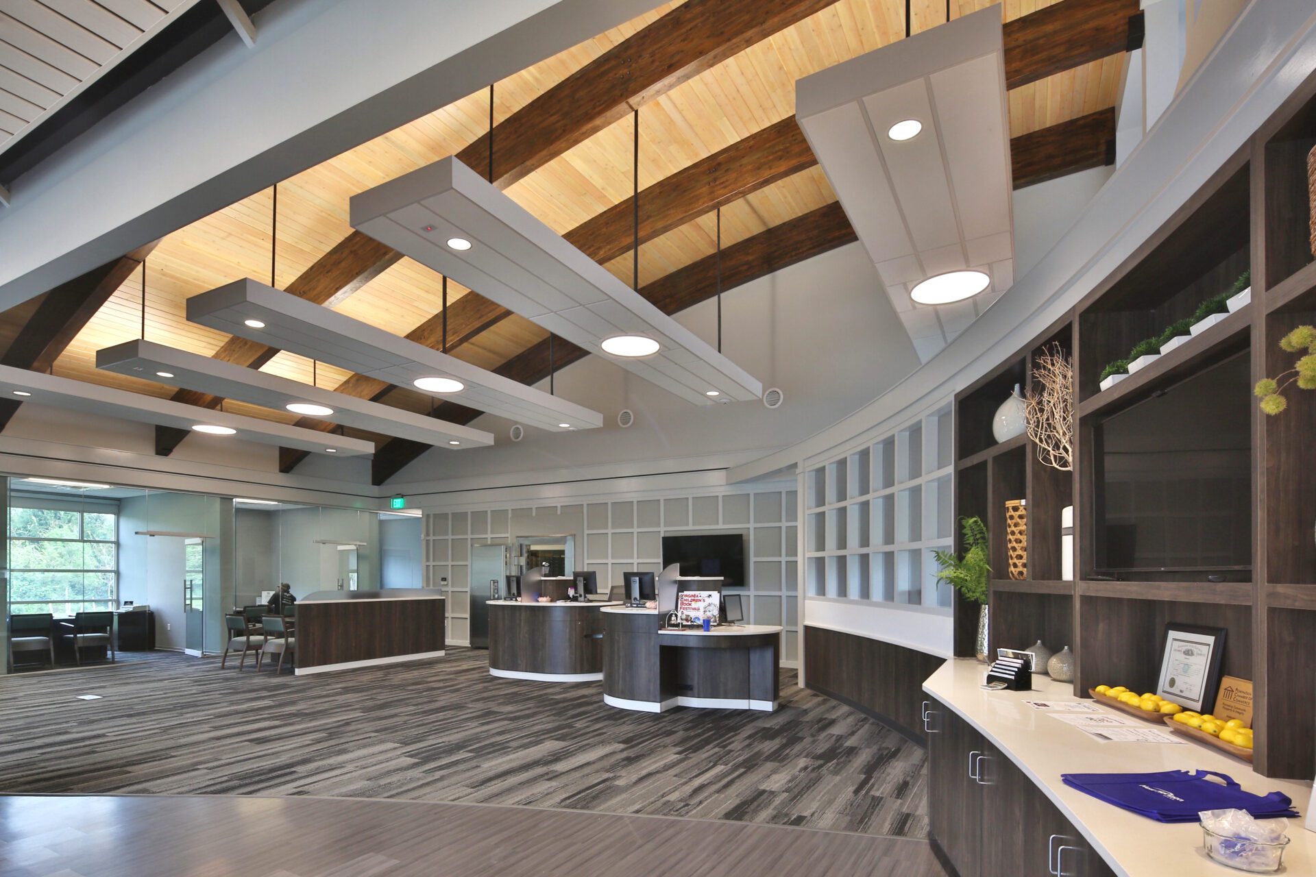 Modern office lobby with wooden ceiling beams, recessed lighting, and minimalist furniture