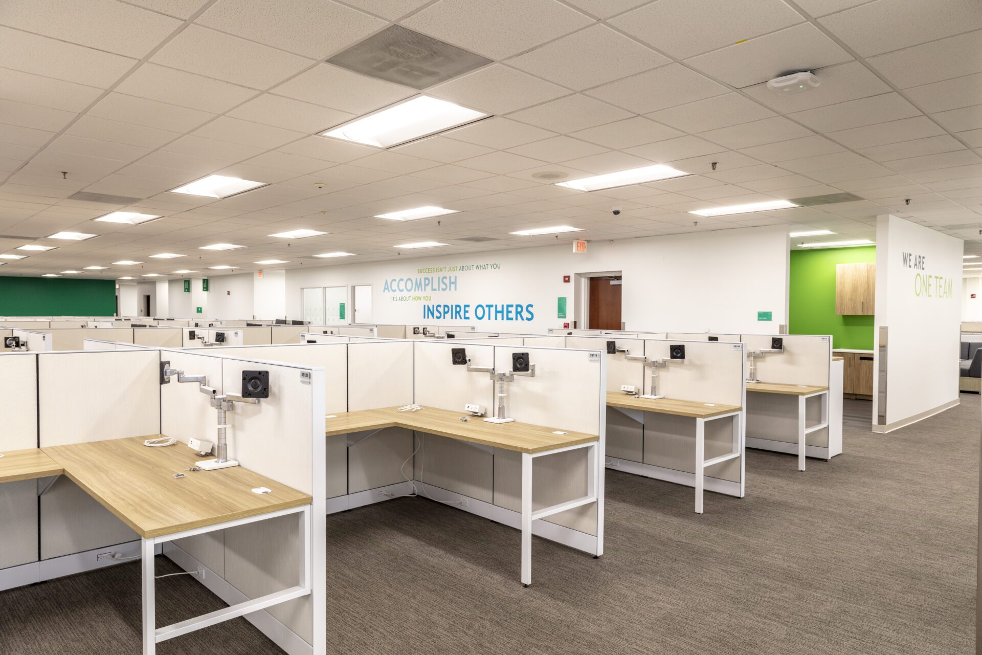 Modern office space with empty cubicles, motivational slogans on walls, and green accents