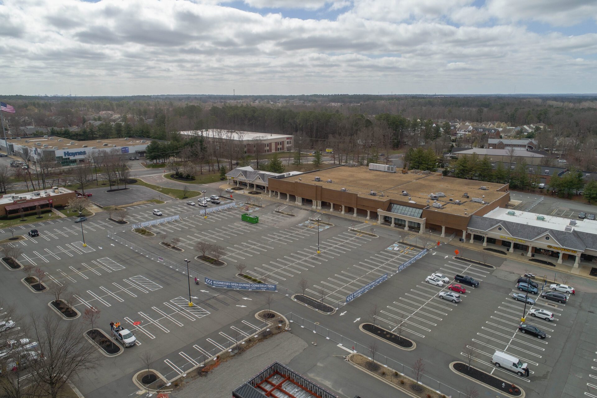 Aerial view of a partially filled parking lot at a shopping center with surrounding trees