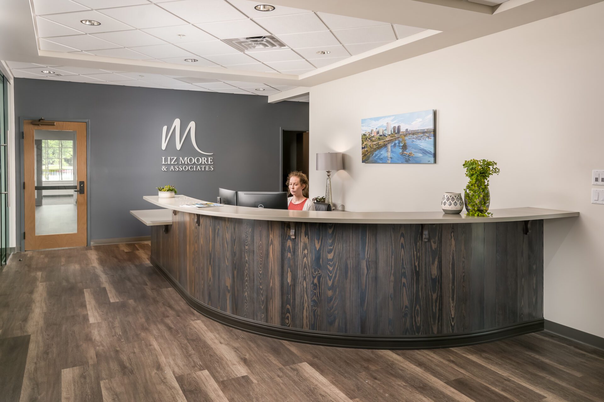 Modern reception area with a curved desk, a landscape painting on the wall, and potted plants