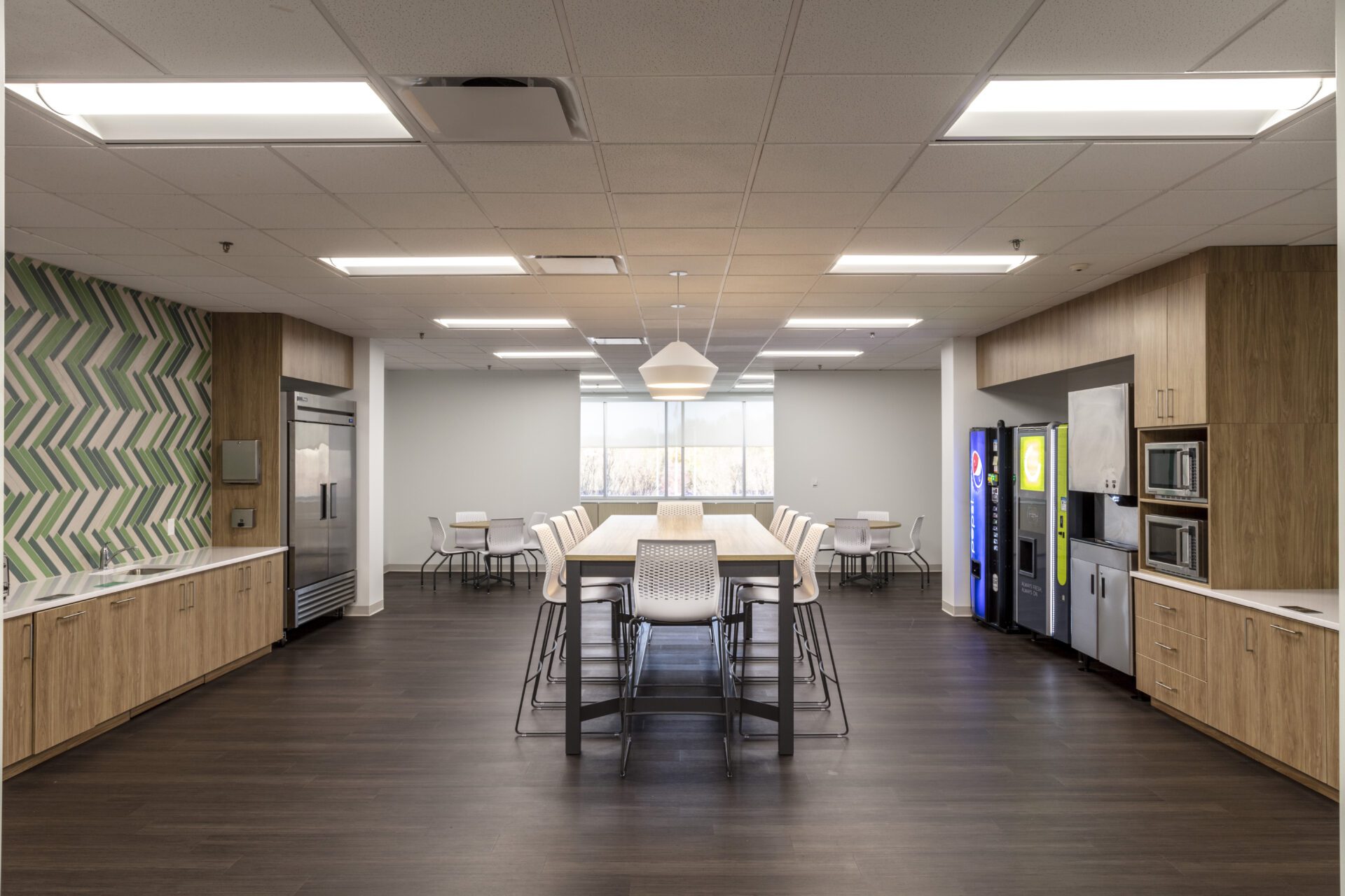 Modern office break room with tables, chairs, and vending machines