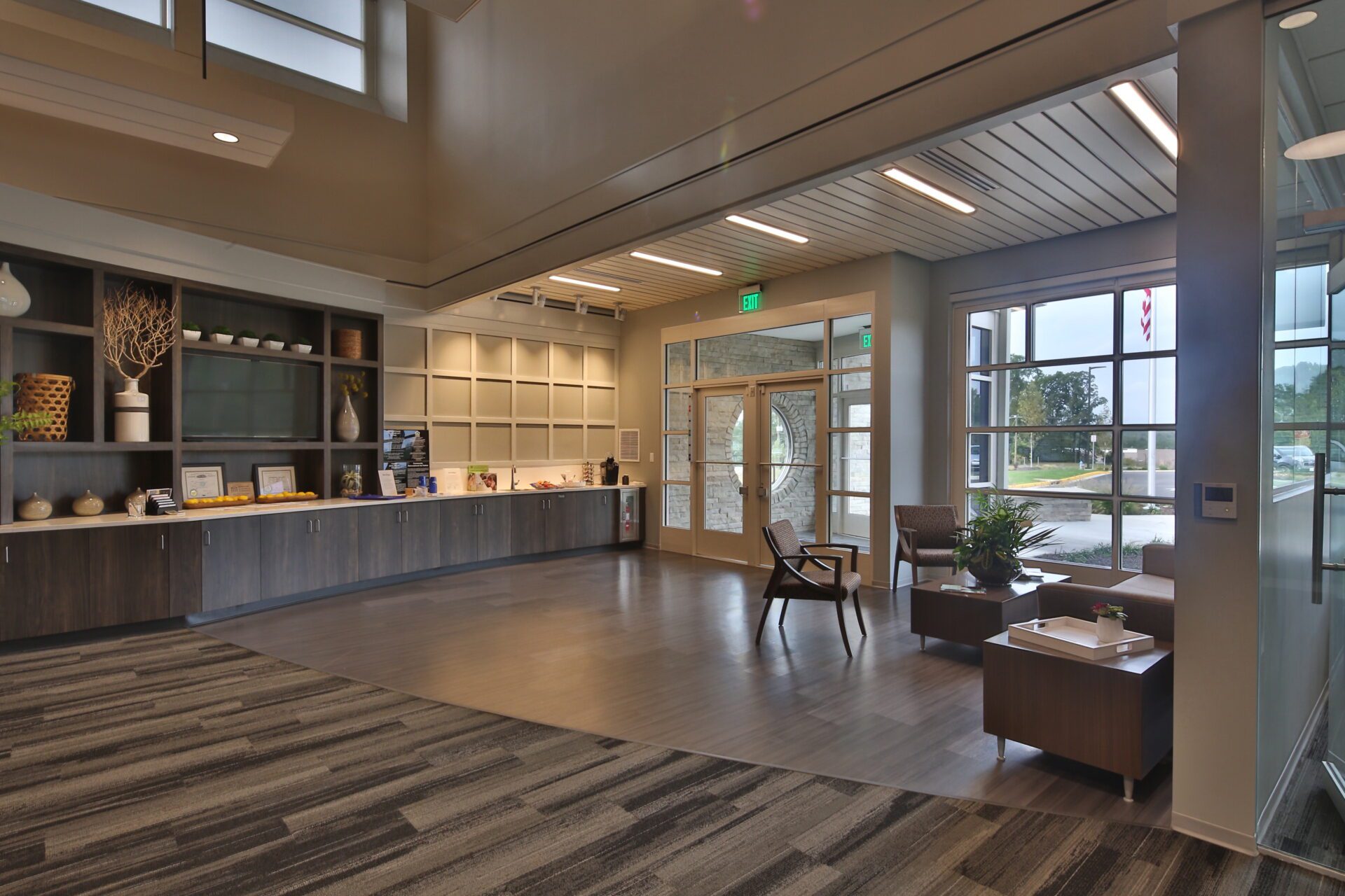 Modern office lobby with wooden furniture, shelves with decorative items, and large windows