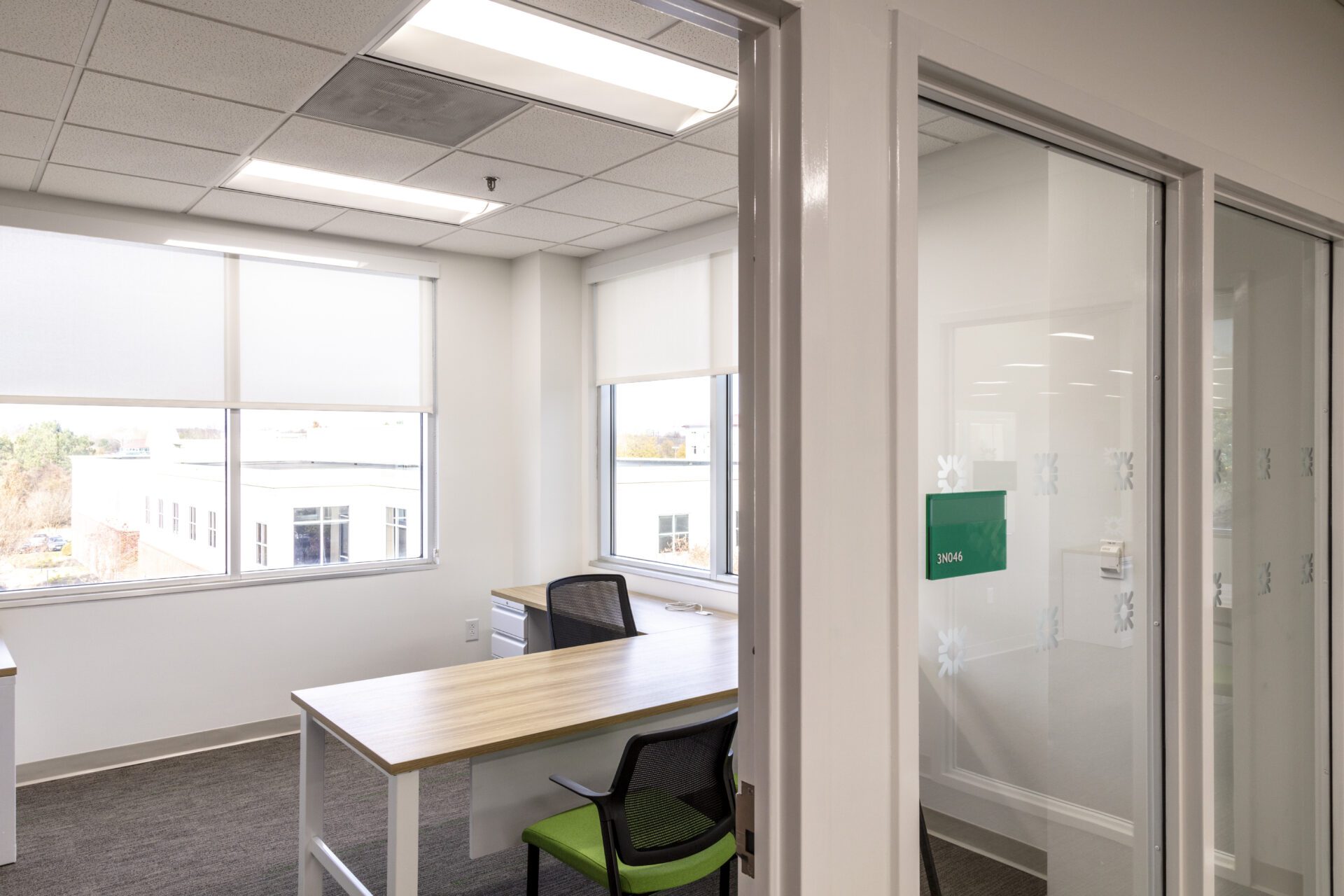 Bright modern office with desk, chair, and large window, viewed through a glass door