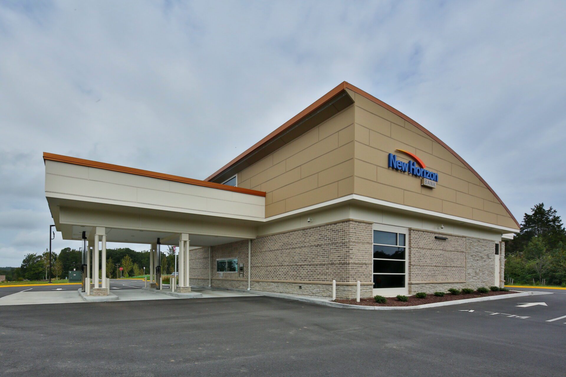 Exterior of New Horizon Bank building with clear signage, parking lot in the foreground, and overcast sky