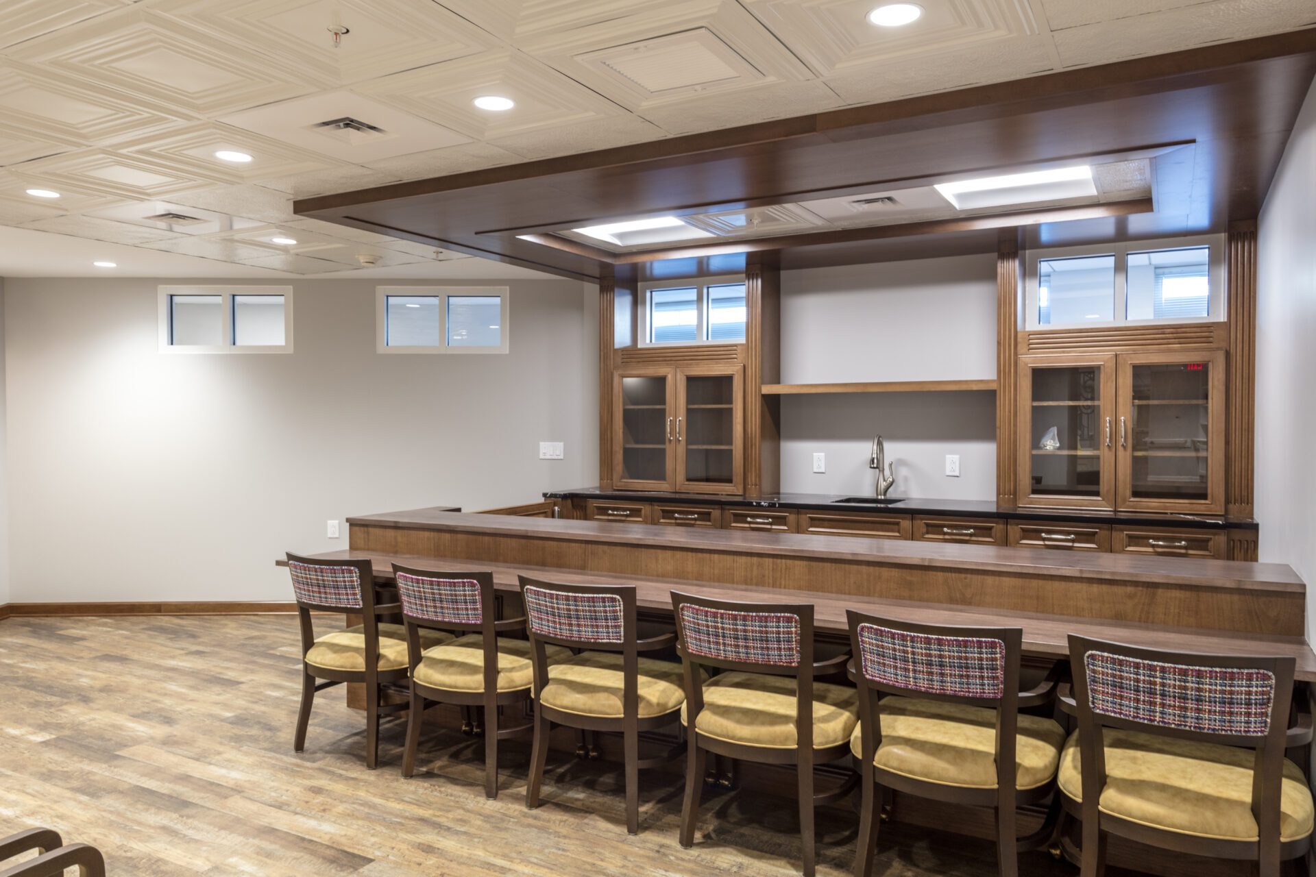 Modern kitchenette with wooden cabinets, bar counter, and patterned stools in a room with decorative ceiling