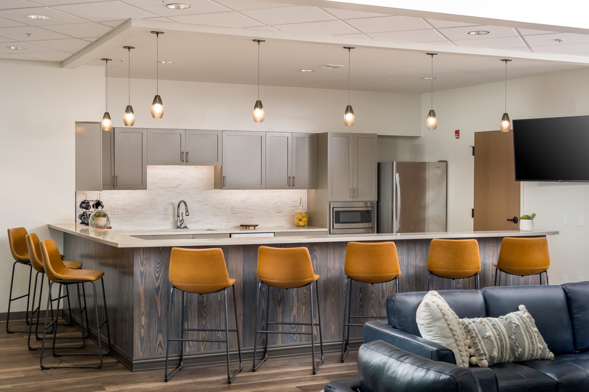 Modern kitchen with bar stools, pendant lighting, and a living area with a dark couch