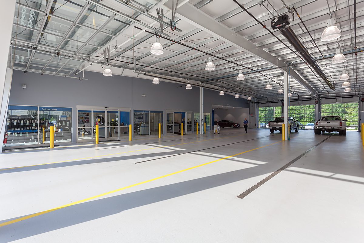 Bright, spacious vehicle service center with large glass front, high ceilings, and several parked cars