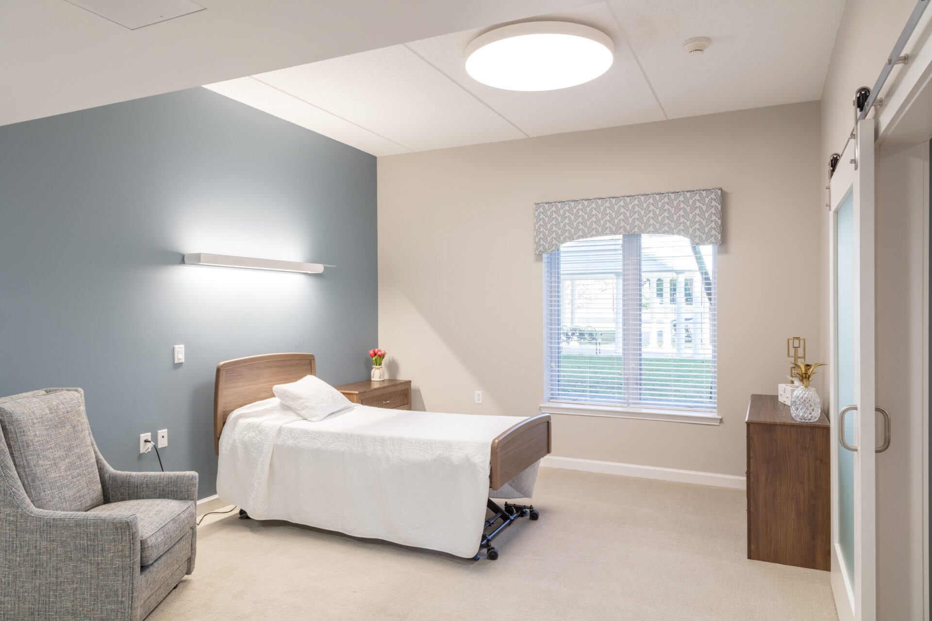 Modern room with a bed, armchair, and window with blinds.